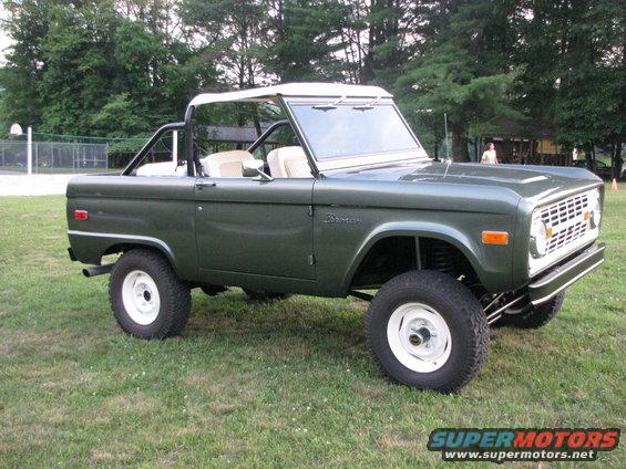 Green 1979 Ford Bronco with white wheels and soft top, parked on grass