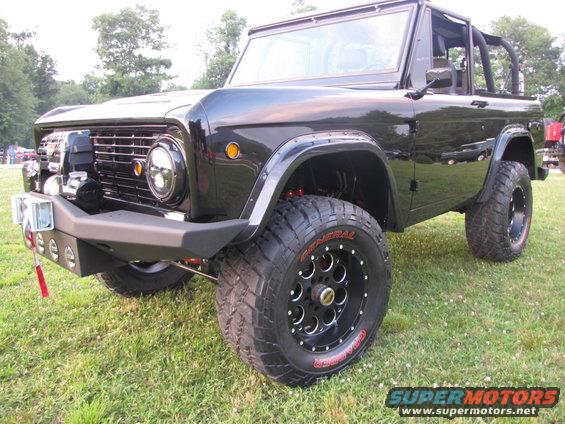 Black Ford Bronco with aftermarket bumper and large tires parked on grass