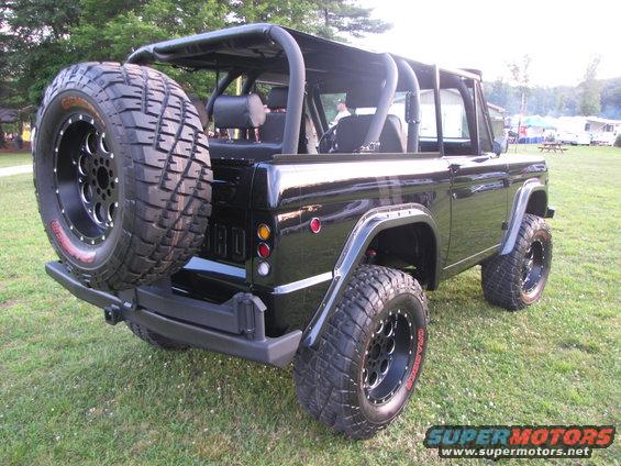 Black Ford Bronco with aftermarket wheels and tires, spare tire on rear, roll cage visible