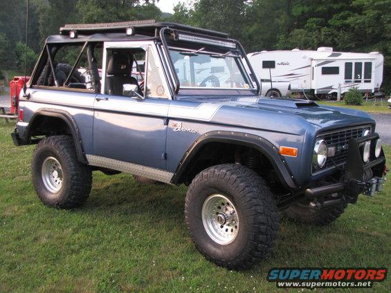 Blue 1978 Ford Bronco with roll cage, light bars, and large off-road tires parked on grass