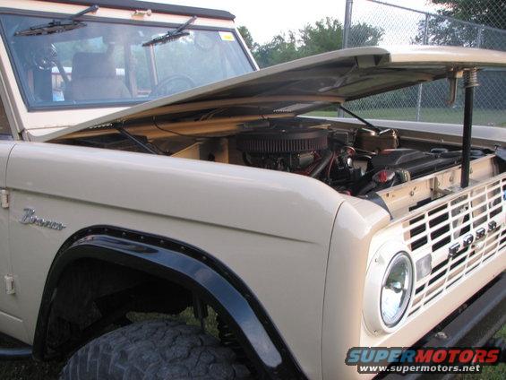 Tan Ford Bronco with hood open showing engine. Bronco script on fender