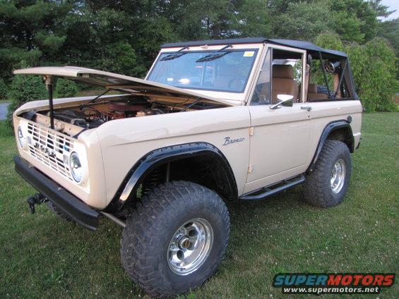 Tan Ford Bronco with hood open, showing engine. Off-road tires and black fender flares