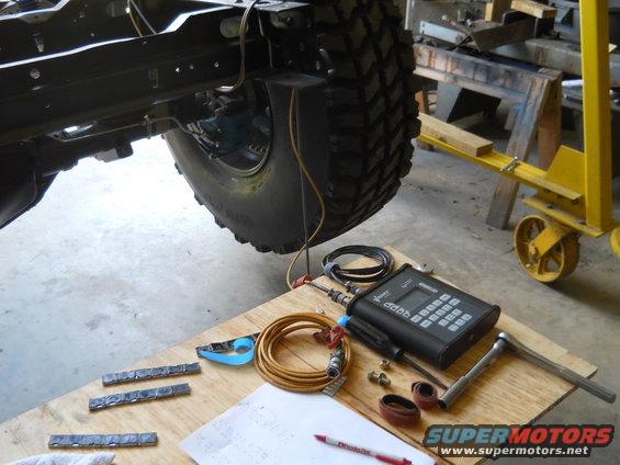 Close-up of vehicle frame and tire with diagnostic tools and paperwork on a wooden surface