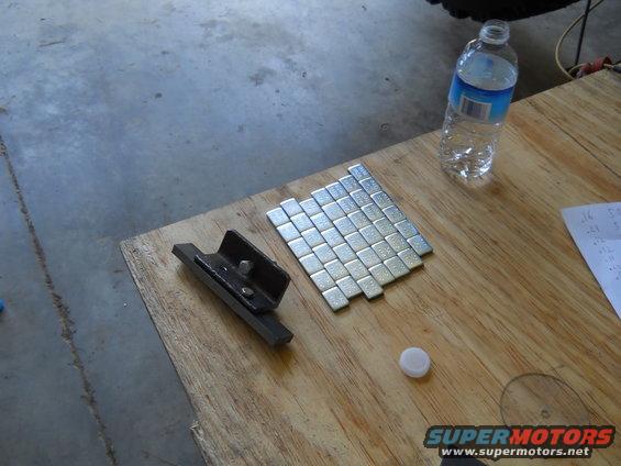 Wheel weights and a metal bracket on a wooden surface. Water bottle nearby