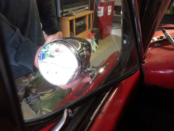 Chrome side mirror being held near the A-pillar of a red car