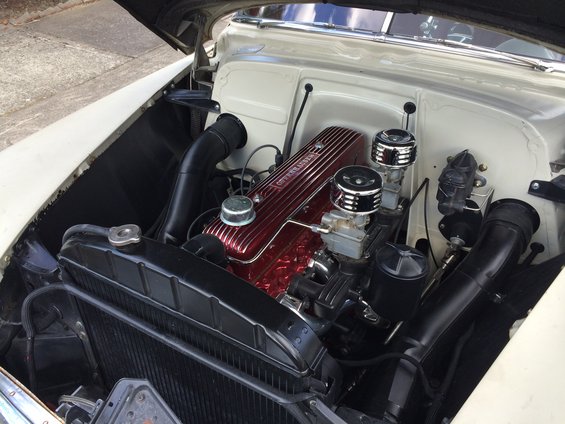 Close-up of a car engine with a red valve cover and dual carburetors