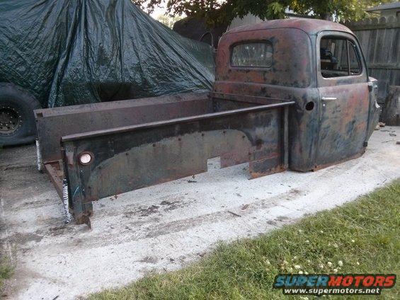Rusty pickup truck cab and bed sitting on concrete, partially covered by a tarp