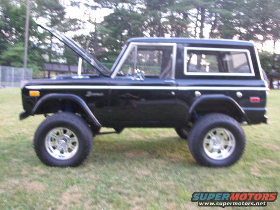 Black Ford Bronco with hood open, lifted suspension, and aftermarket wheels parked on grass