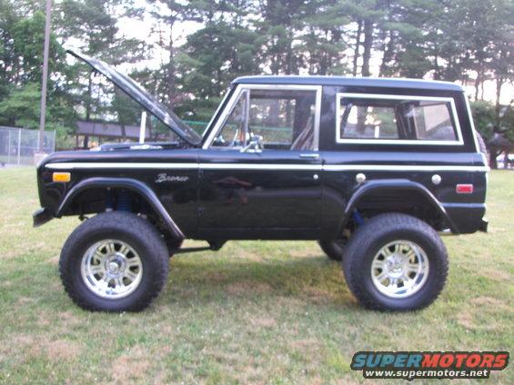 Black 1978 Ford Bronco with hood open, lifted suspension, and chrome wheels parked on grass