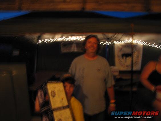 Two people stand under a tent with string lights; one holds stacked documents