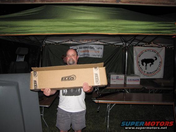 Man holding a box with ECGS logo under a tent with early broncos banners