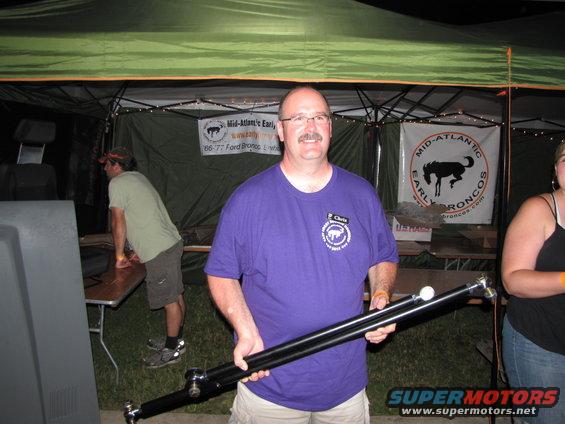 Man in purple shirt holding a driveshaft, with a banner for Mid-Atlantic Early Broncos in the background