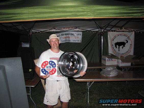 Man in hat and t-shirt holding two chrome wheels and US Made stickers. Banner behind him says Mid-Atlantic Earl Broncos