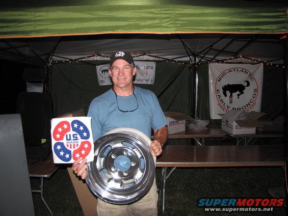Man holds a shiny metal wheel and a sticker with red and blue stars and 'U.S. MAGS'