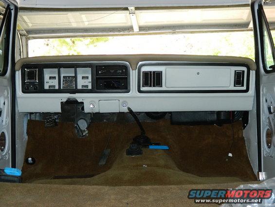 Vehicle dashboard with gauges, radio, and vents. Brown carpet covers the floor