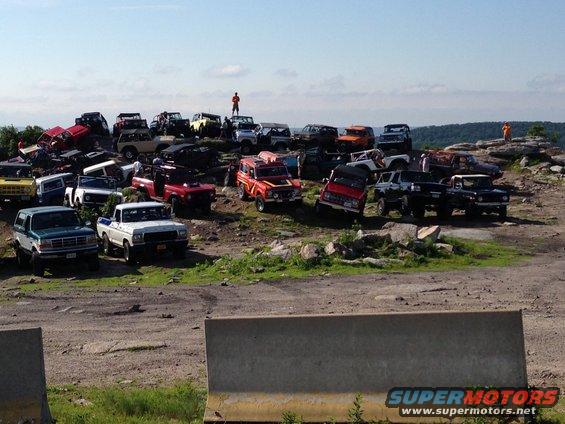many off-road trucks and SUVs parked on a rocky hill under a clear sky