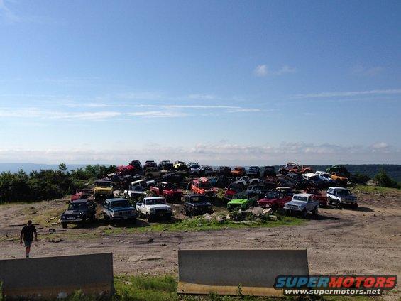 Junkyard scene with dozens of SUVs and trucks piled on a hill under a blue sky