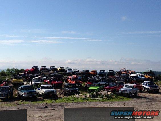 many SUVs and trucks piled up on a hill under a blue sky