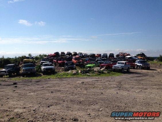 Junkyard scene with numerous trucks and SUVs parked on a hill under a blue sky