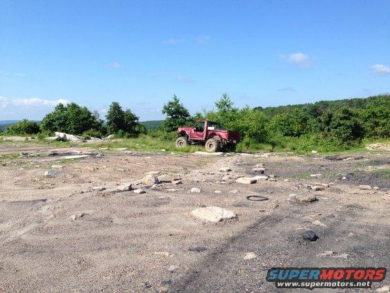 red pickup truck with large tires parked on rocky terrain with trees in background