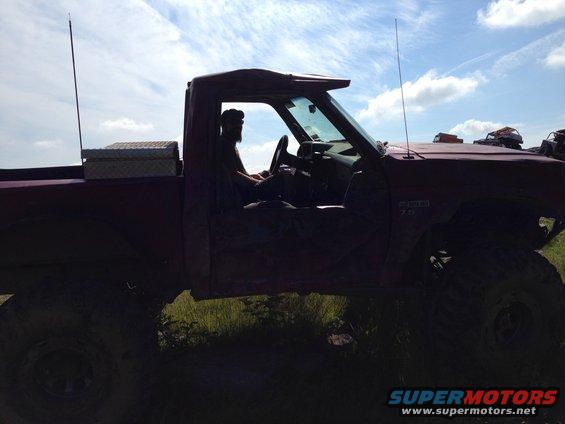 Side view of a red pickup truck with lifted suspension, driver visible inside. Text on fender reads 'RANGER 7.3'