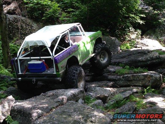 Green and purple off-road vehicle with a white canopy and roll cage navigating rocky terrain