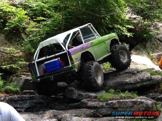 Green off-road vehicle with white roll cage and canopy climbing over large rocks