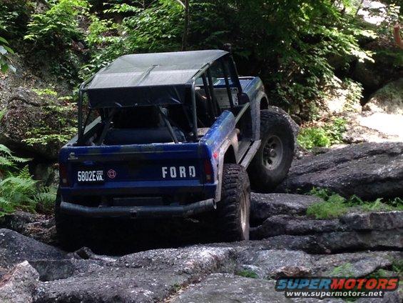 Blue Ford Bronco navigating rocky terrain, rear view