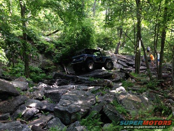 Dark blue off-road vehicle with a roll cage navigating a rocky trail