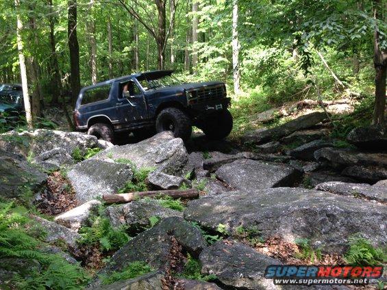 Dark blue 1987 Ford Bronco navigating a rocky trail in a forest