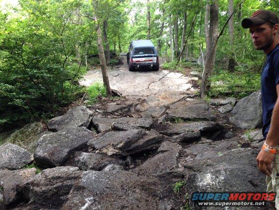Dark SUV navigating a rocky trail in a wooded area