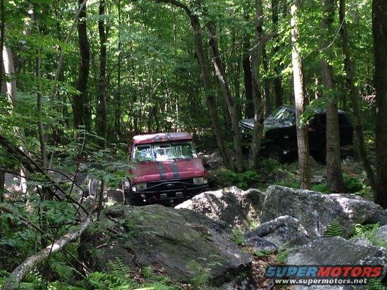 Red off-road vehicle with black stripes on hood, navigating rocky terrain