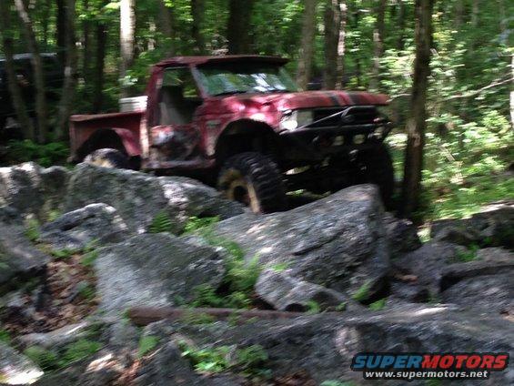Red pickup truck with off-road modifications navigating rocks