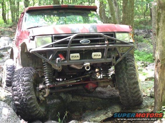 Red off-road SUV with custom bumper and PIAA lights, angled front view on rocky terrain