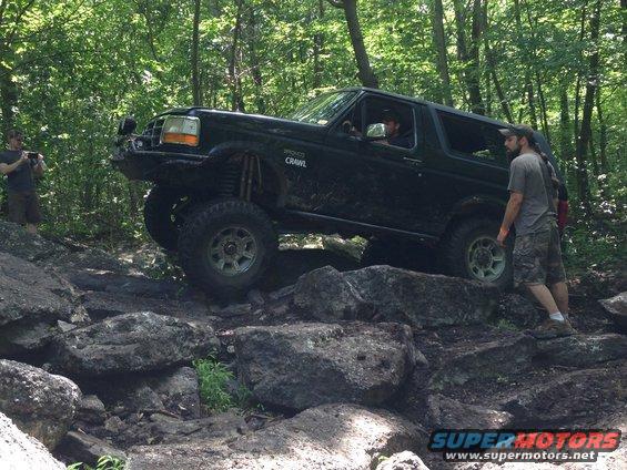 Black Ford Bronco off-roading over rocks, lifted suspension, aftermarket bumper
