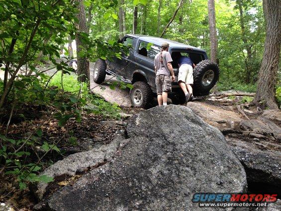 Dark Ford Bronco navigating rocky terrain, rear view with spare tire visible