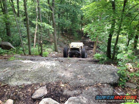 Yellow off-road buggy climbing a rocky trail in a forest