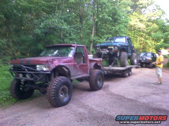 Red pickup truck towing a green SUV on a trailer, off-road tires
