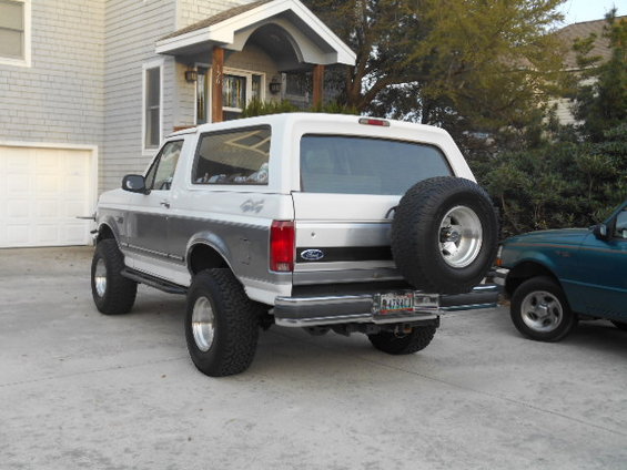 White and grey Ford Bronco with lifted suspension and spare tire on rear door, parked on concrete