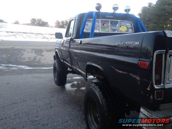 Black pickup truck with a blue roll bar and lights on top. Has 'Custom' badging on the side