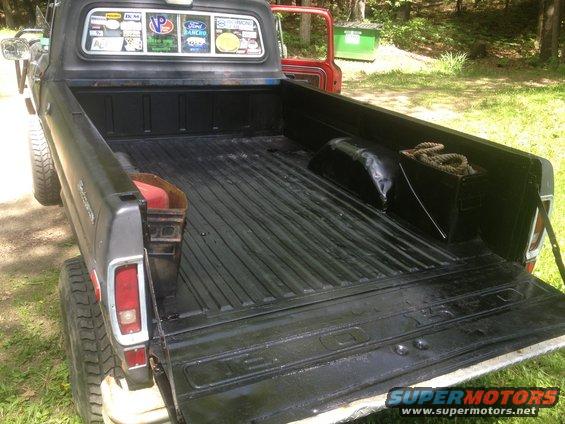 Rear view of a 1973 Ford F-100 pickup truck bed with a black liner and a red door open