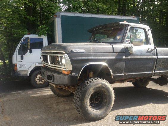 Black 1970 Ford F-250 pickup truck with large tires, parked next to a white box truck