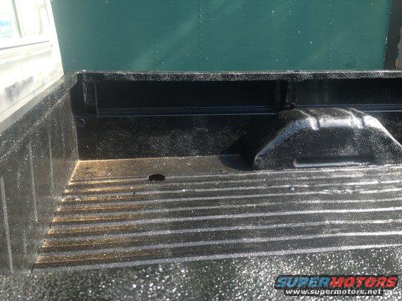 Truck bed with black spray-in liner. Green wall behind it
