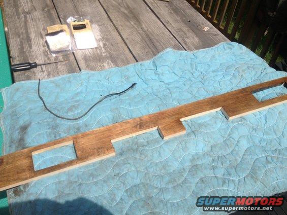 Wooden dashboard trim with cutouts, on a blue quilted mat, with a screwdriver and hardware