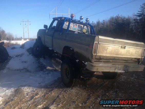 Ford pickup truck with a blue roll bar, driving on a snowy, muddy incline