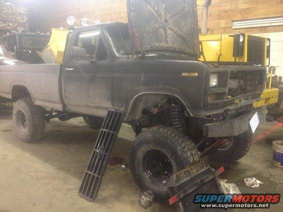 Black Ford F-Series pickup truck with hood open, missing grille, and lifted suspension