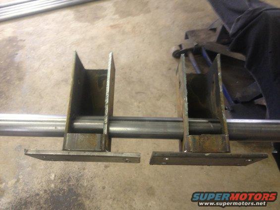 Two custom metal brackets welded onto a pipe, with mounting plates below