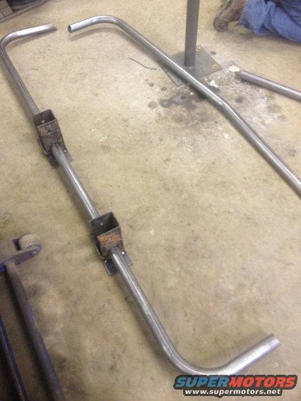Metal tubing with square brackets welded on, lying on a concrete floor
