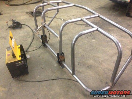 Metal roll cage frame under construction with welding equipment nearby