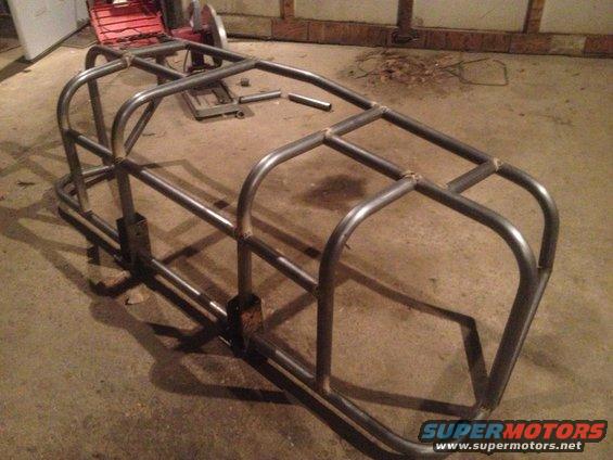 Bare metal custom roll cage frame with welded tubing, sitting on a concrete floor